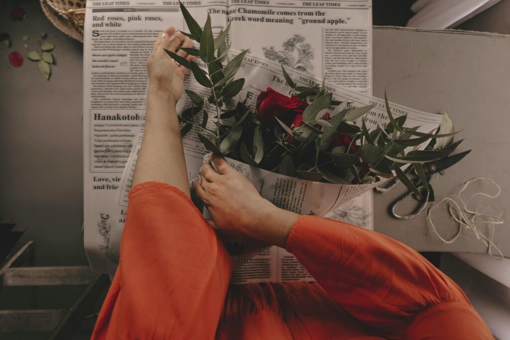 A woman in red dress arranges roses on newspaper, creating a floral arrangement.